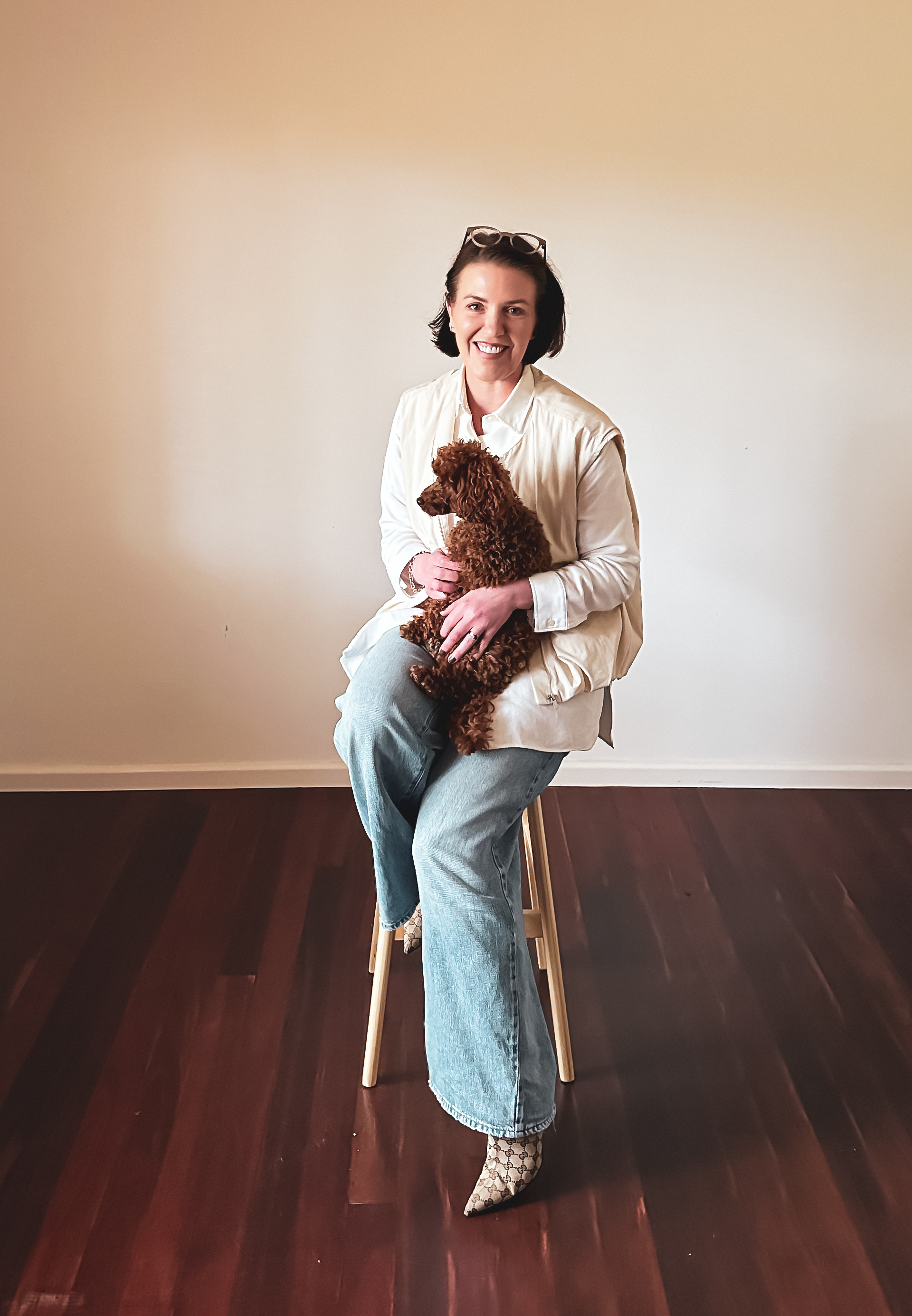 Belinda Hendrickson, host of She Jumped Anyway, seated on a stool holding her dog
